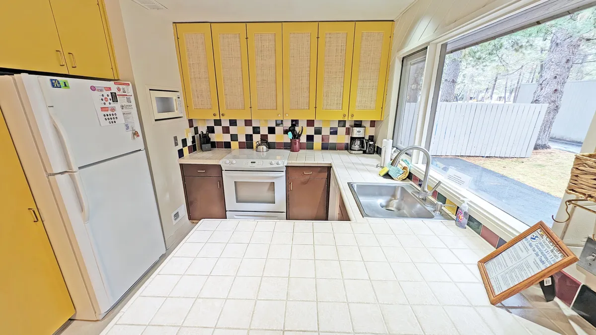 A bright and cheerful kitchen featuring yellow cabinetry, a checkerboard backsplash, and a large window that lets in abundant natural light. The space is practical yet visually inviting, making it perfect for family meal prep and casual morning coffee.