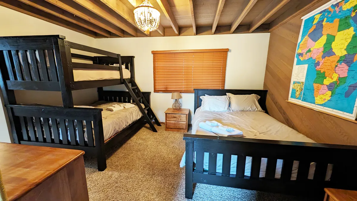 A cozy, inviting space with bunk beds, a single bed, playful decor including a world map, and a chandelier. The open design suggests a fun, communal atmosphere ideal for kids or groups.