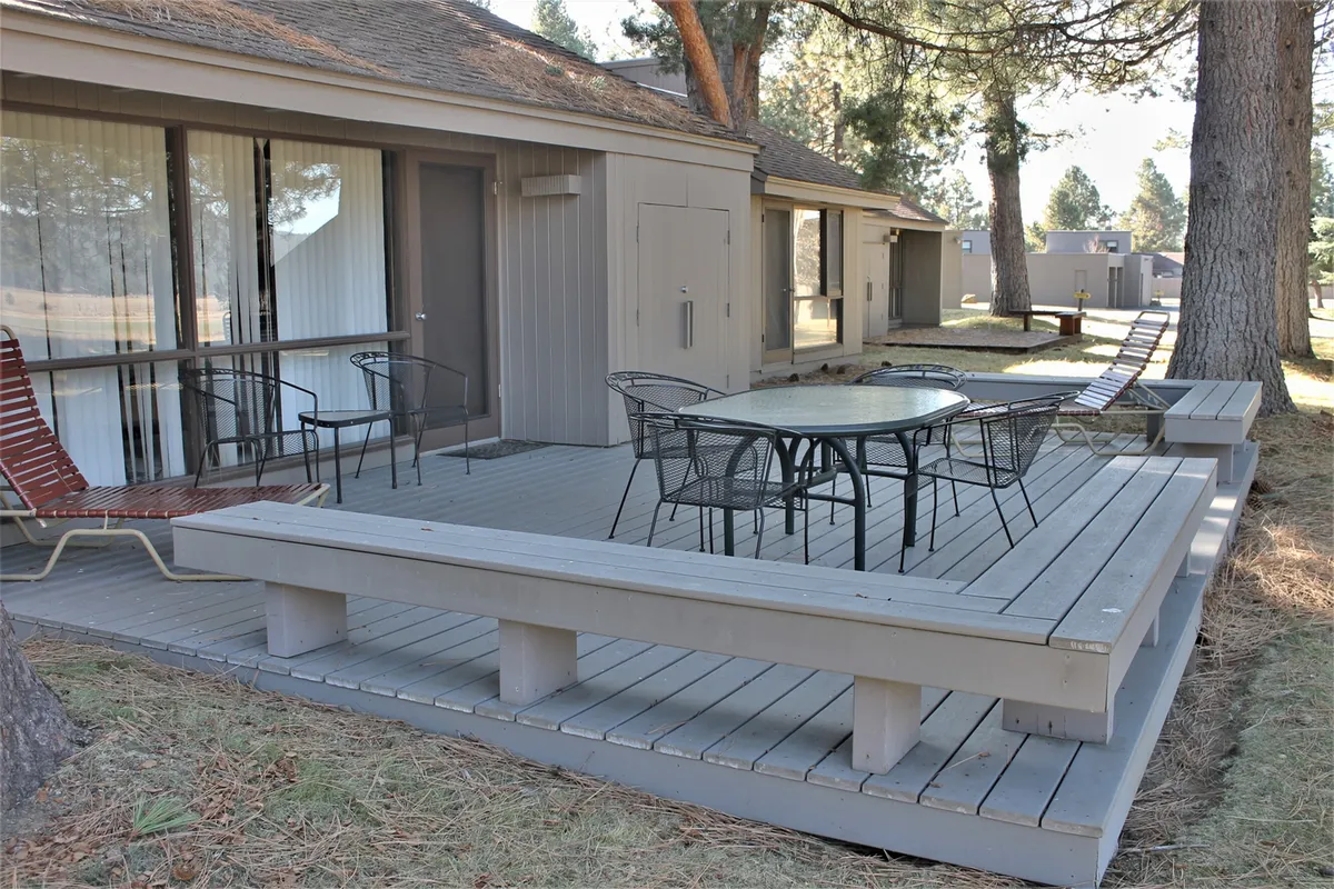 A welcoming outdoor seating area on a wooden deck, featuring a round glass table surrounded by comfortable chairs. The setting is nestled among trees, suggesting a serene spot for relaxing after outdoor adventures.